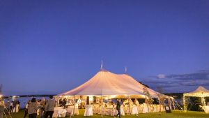 A brightly lit outdoor tent on grassy field under a partly cloudy evening sky
