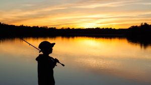 Silhouette of a young child holding a fishing pole and looking out at a body of water