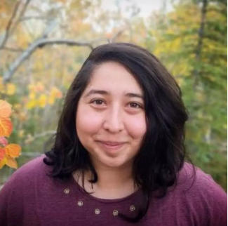 A smiling person standing in a forest