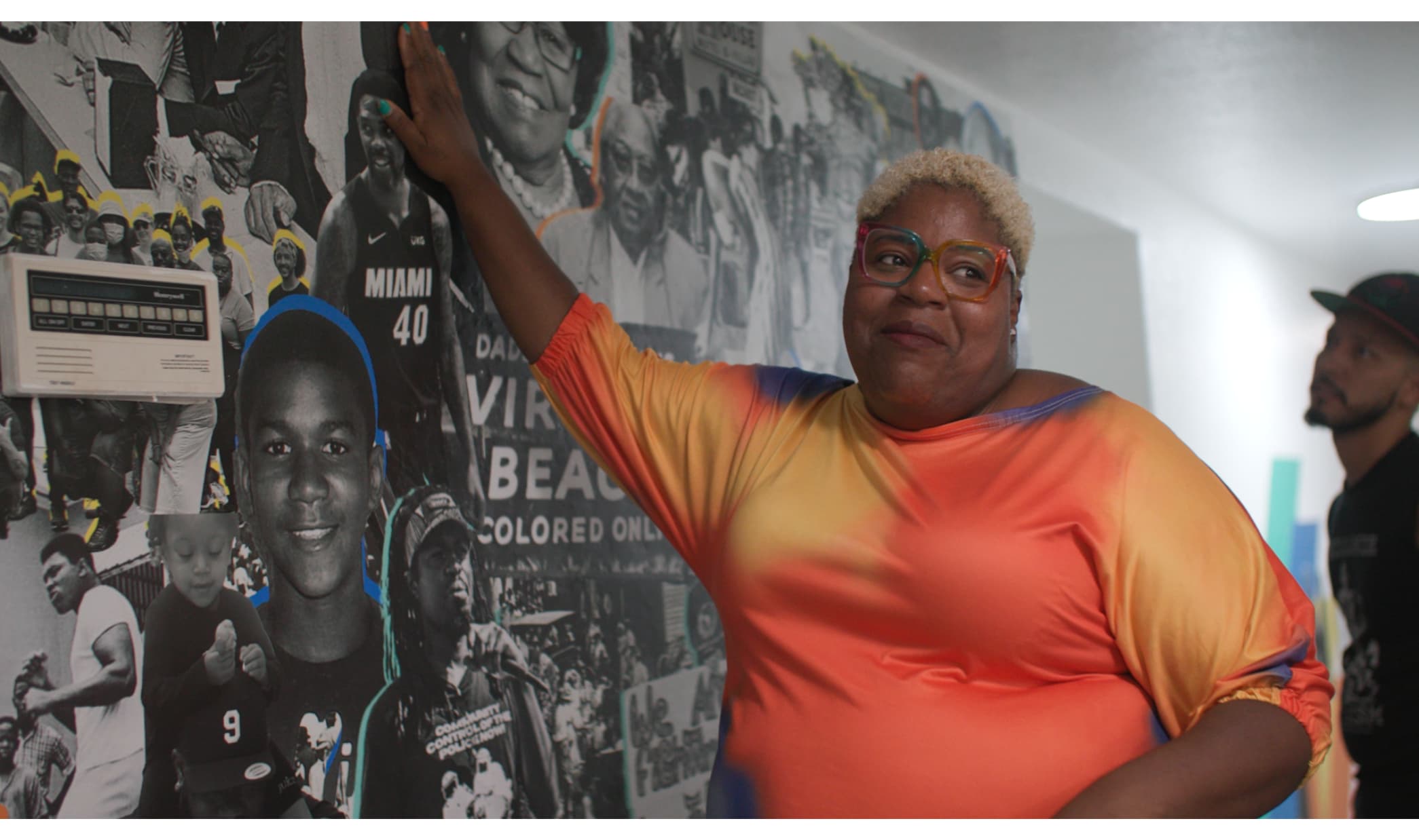 Photo of Valencia Gunder raising a hand to a mural filled with photos of Black leaders in history