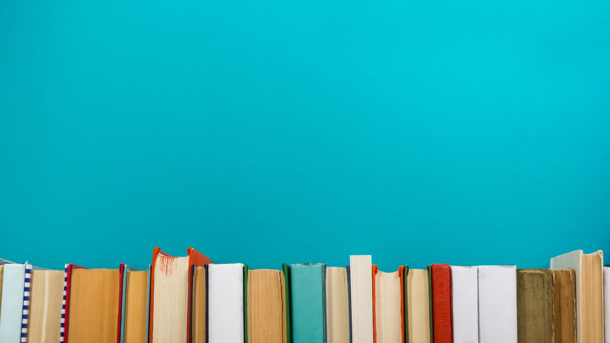 A row of multicolor books run along the bottom of the photo with a bright teal wall above them. 