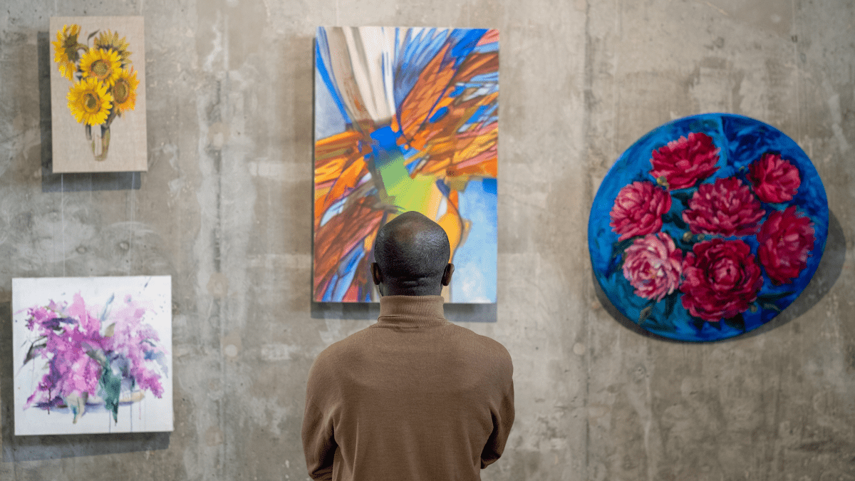 Back view of African male guest of art gallery standing in front of wall with expositions and looking at one of them