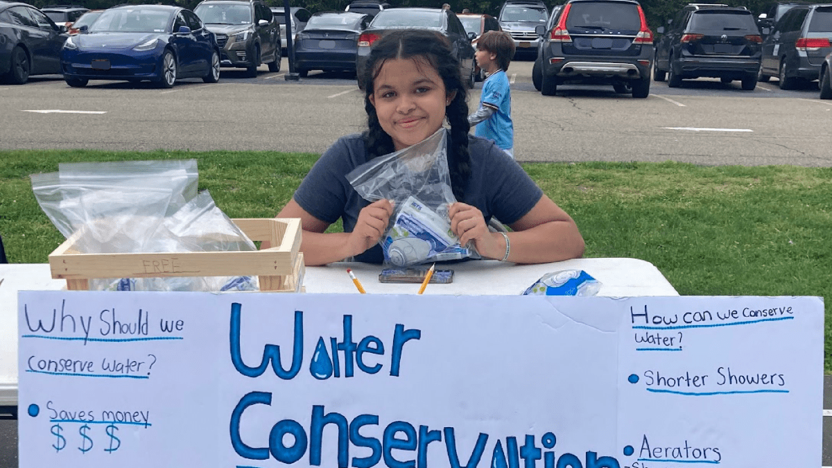 Student sits at a table behind a poster titled, "Water Conservation"