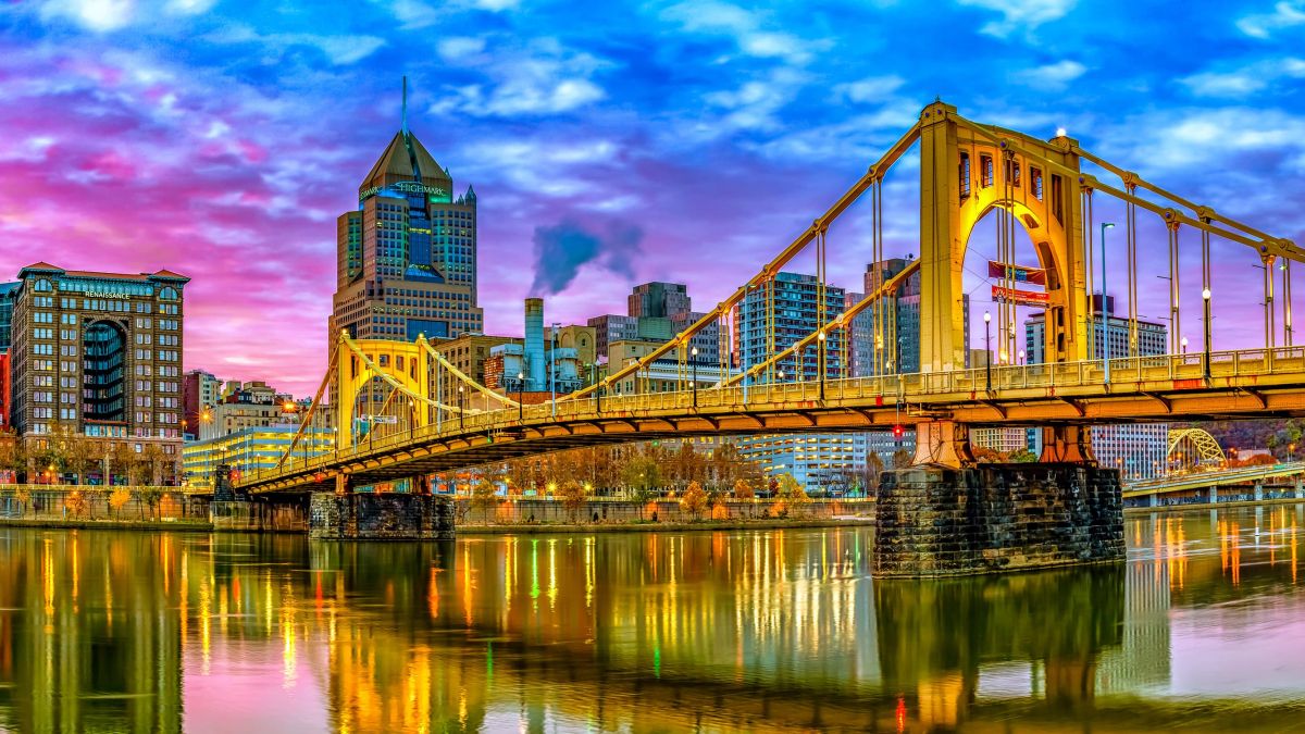 Landscape photo of yellow bridge over body of water and city skyline at sunset