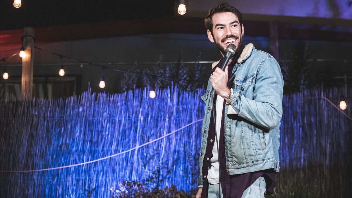 Esteban Gast wears a jean jacket and holds a mic in front of a crowd. Photo by Andrew Max Levy