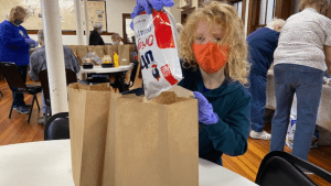 Child wearing face mask and gloves helps to bag food to hand out at the food pantry. 