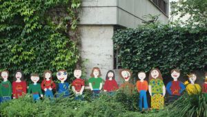 Background is an ivy-covered building and lined up in front of the building are paper cutouts of smiling people