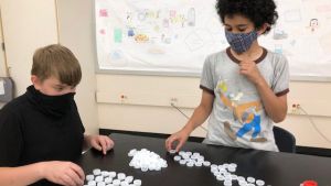 Three masked students count and sort bottle caps during afterschool program.