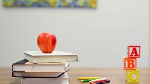 Image of an apple sitting on books on a desk with colored pencils.