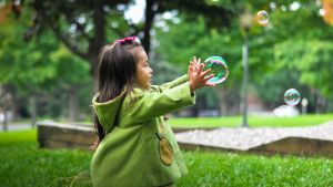 Child, wearing green, reaches for a bubble. 