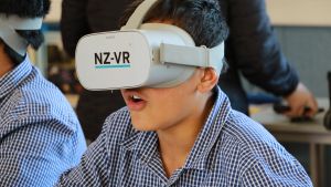 a young student sitting at a desk wearing a white VR headset with NZ-VR on it
