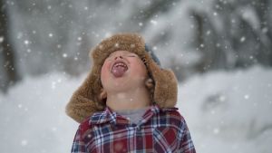 Photo of a young child facing the sky and trying to catch snowflakes