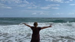 Girl with arms stretched towards the sky, standing in shallow waves in an ocean