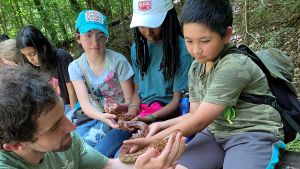 A group of young students hold a snake with guidance from an educator