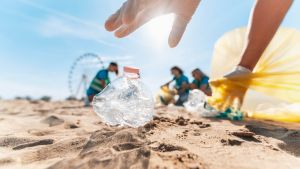 Worm's eye view of a pair of hands picking up plastic trash on beach, and in the background is a blurry group of three other volunteers and a ferris wheel