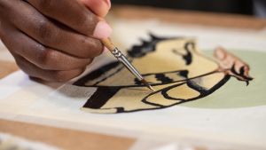Close-up of a Black artist painting a butterfly on paper