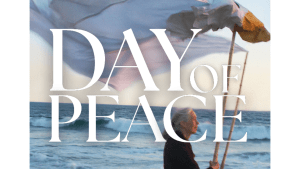 Jane Goodall holds a giant peace dove puppet near the ocean. DAY OF PEACE is written over the image.