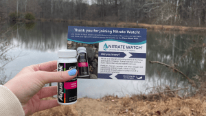 a volunteer holds their Nitrate Watch kit in front of a body of water