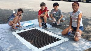 Four smiling students stencil a storm drain.