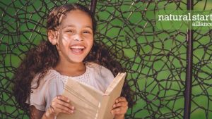 green background with little girl smiling in forefront with a book in hands