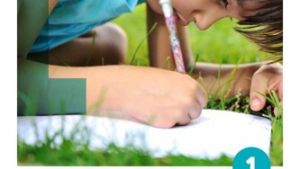 A young child writing on paper lying on grass