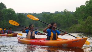 Two kids in an orange kayak paddle on a river