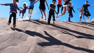 A group of kids jumping on a sand dune
