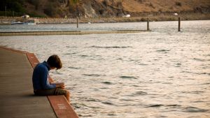 Middle school student sitting at lakeshore reading book 