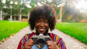A smiling Black woman holding a camera in a park