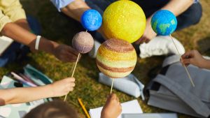 Close-up of a group of children holding model planets while enjoying outdoor astronomy class outdoors in sunlight