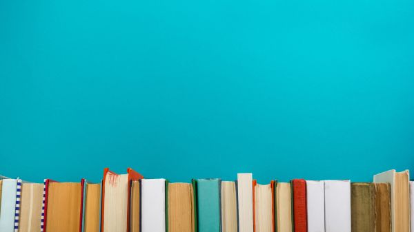 A row of multicolor books run along the bottom of the photo with a bright teal wall above them. 