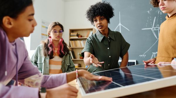 Teacher gestures at solar panels to three students