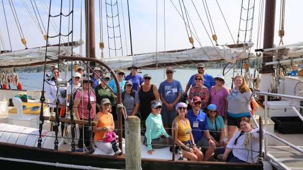 A group of teachers smile while sitting on the deck of a tallship schooner.