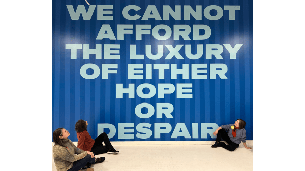 Course Facilitators sitting by a mural that reads 'We cannot afford the luxury of either hope or despair'