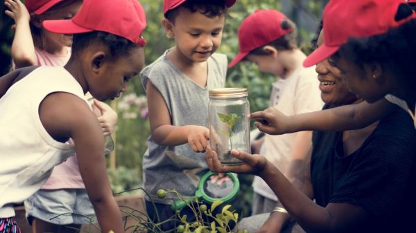 Kids outside looking at a glass jar held out by their teacher 