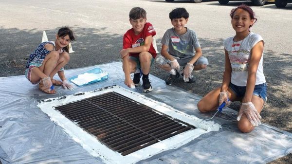 Four smiling students stencil a storm drain.