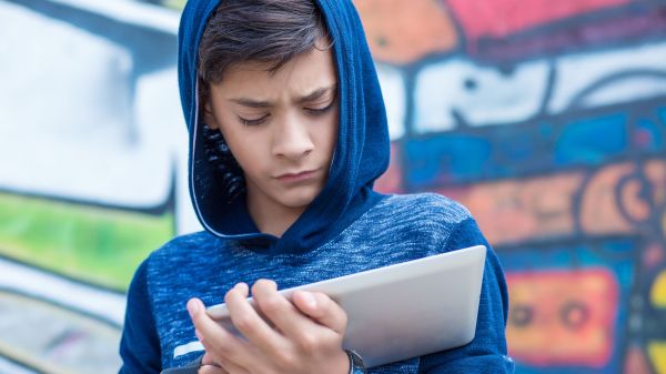Young person in blue hoodie looking at tablet.