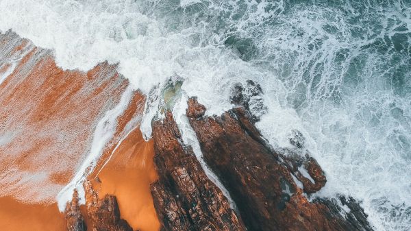 Aerial photo of a beach with ocean waves crashing on rock
