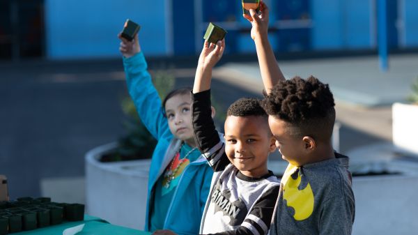 Three young kids hold up stamps. The child in the middle smiles as the other child.