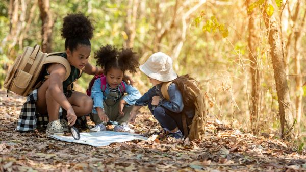 Three kids crouching on a fall-leaf laden forest floor to look at a map.