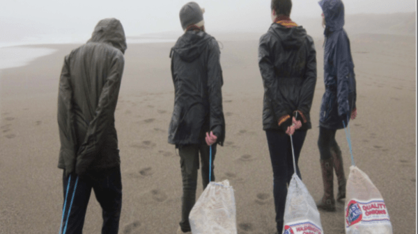 Four people dragging large bags of marine debris across a beach.
