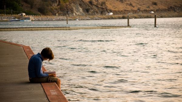 Middle school student sitting at lakeshore reading book 