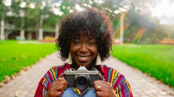 A smiling Black woman holding a camera in a park