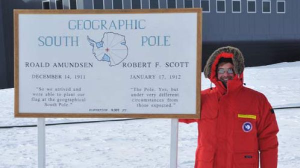 A person stands next to a sign that states "Geographic South Pole"