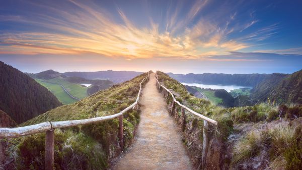 path with railing on mountaintop under sunlit clouds in blue sky