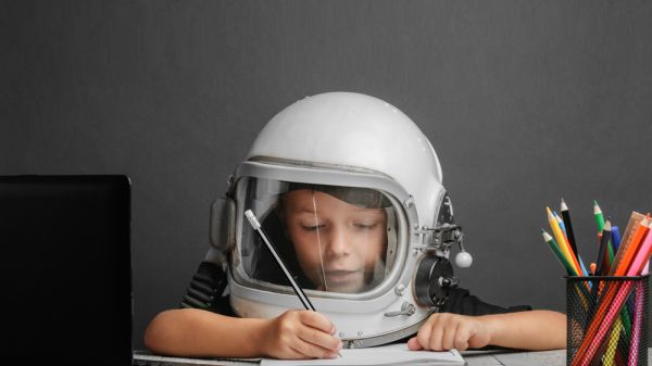 Child wearing an astronaut's helmet and holding a pencil.