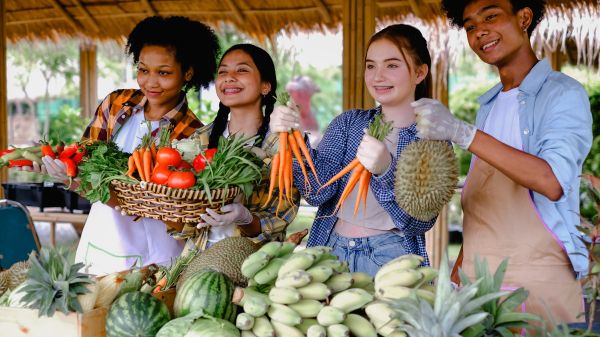 A group of teens holding a variety of vegetables and fruit at a farm outside