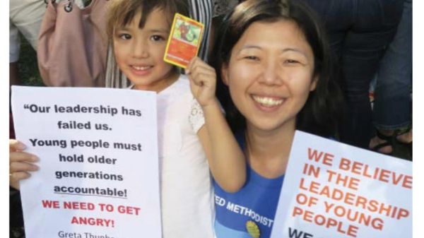 An East American American woman and her daughter at a climate change rally holding signs about faith communities and young people demanding climate action