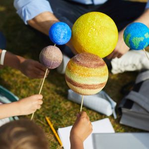 Close-up of a group of children holding model planets while enjoying outdoor astronomy class outdoors in sunlight