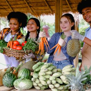 A group of teens holding a variety of vegetables and fruit at a farm outside